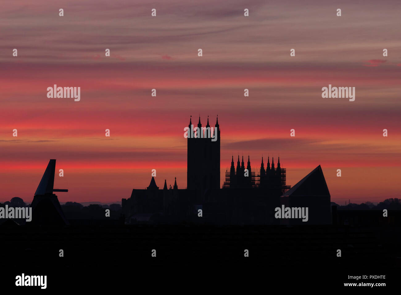 Pink stripey clouds at dawn over Canterbury Cathedral during October. Silhouette of the cathedral plus various Canterbury roofs and an oast house. Stock Photo