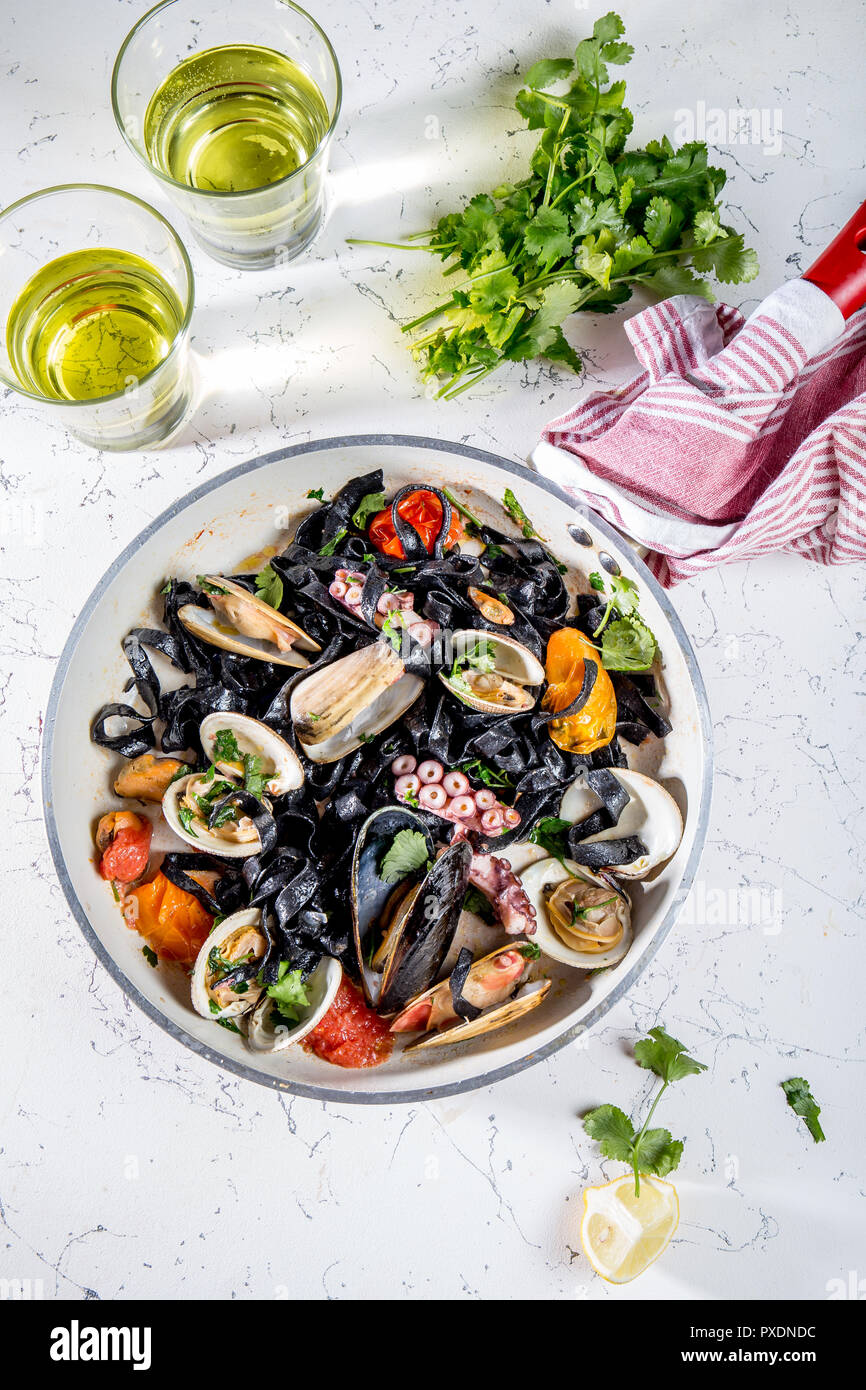 Homemade seafood Black pasta spaghetti with clams mussels octopus vongole in pan with white wine on marbled background Stock Photo