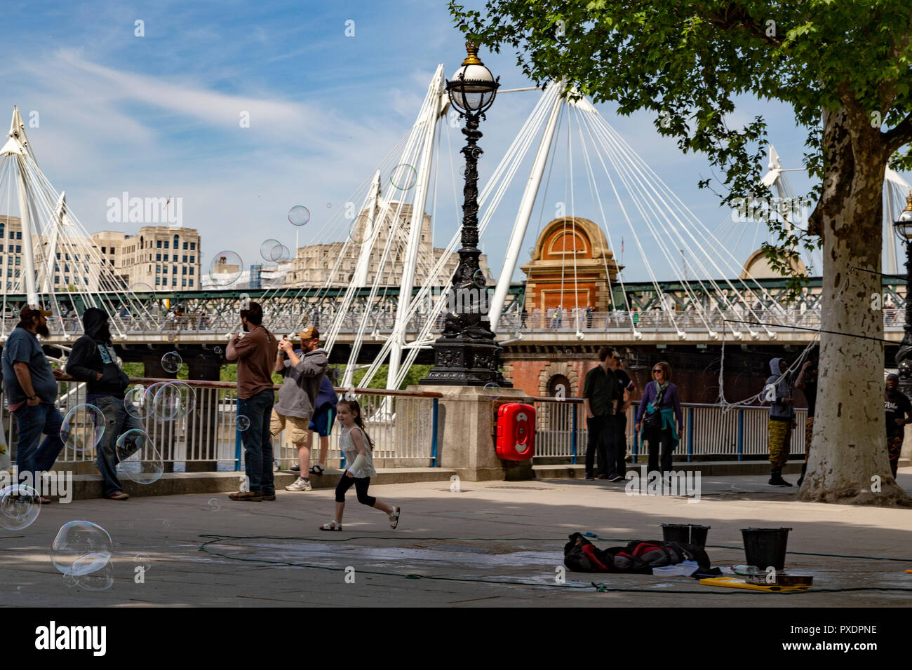 Young girl chasing soap ballons with Hungerford Bridge in the background, London, UK Stock Photo