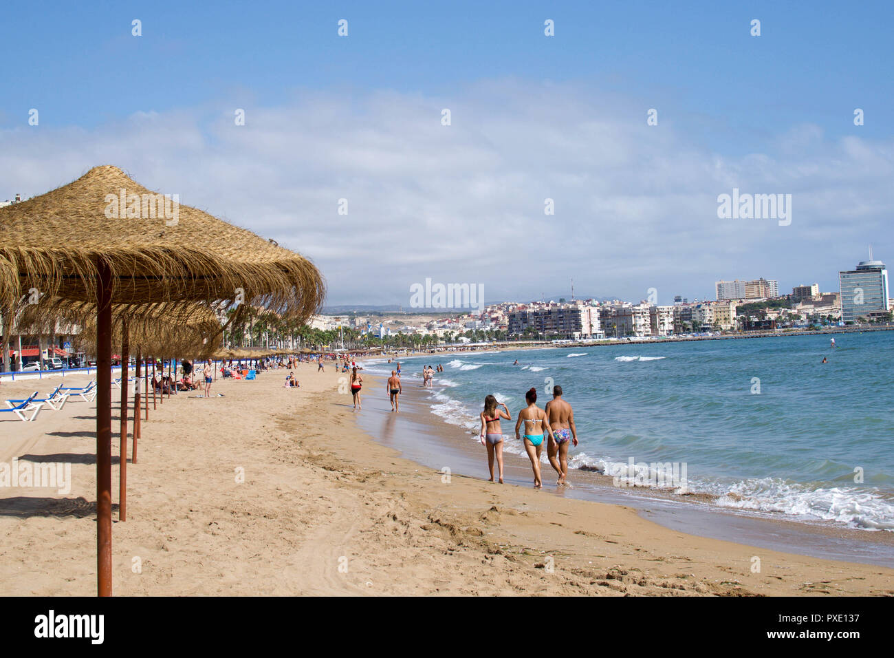 Melilla, Melilla, Spain. 18th Aug, 2018. People are seen walking along the sandy beach in Melilla.The Spanish enclave city of Melilla sits on the North African coast, surrounded on all sides by Morocco and the Mediterranean Sea. The city is surrounded by a 20-foot-tall metal fence to keep out migrants looking to come to Europe, but many migrants make it across anyway. The border is also a thriving economic hub where Moroccan labourers carry goods from Spain into Morocco. Credit: SOPA Images/ZUMA Wire/Alamy Live News Stock Photo