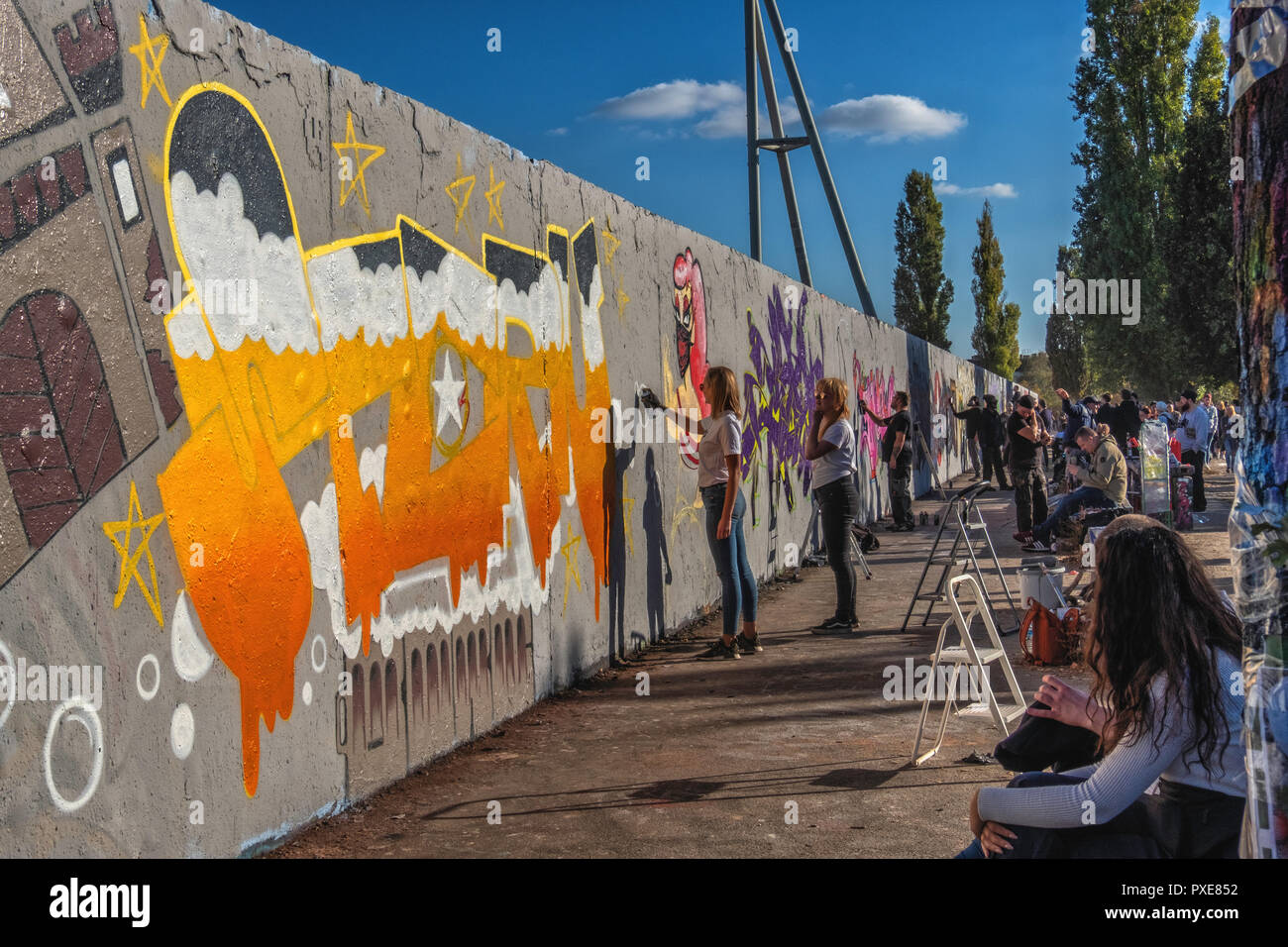 Berlin, Germany, Mauerpark 21st October 2018. Street artists redorate the historic strip of Berlin Wall. Painters  at work creating a long artistic advertisement for Sternburg beer. Stock Photo