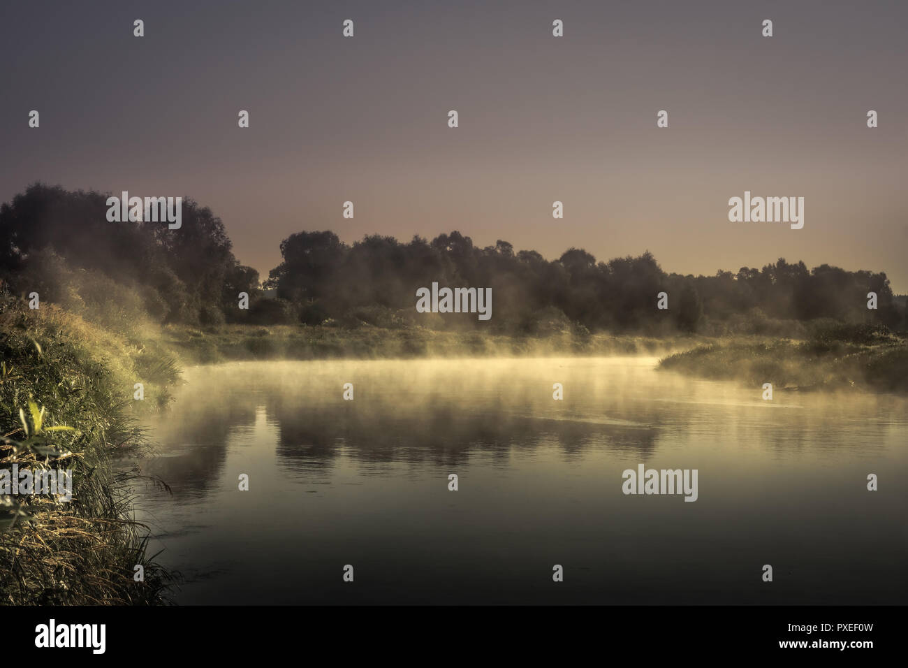 countryside morning sunrise river mist scenery landscape  with tranquil foggy water mirror and dark dramatic moody sky Stock Photo