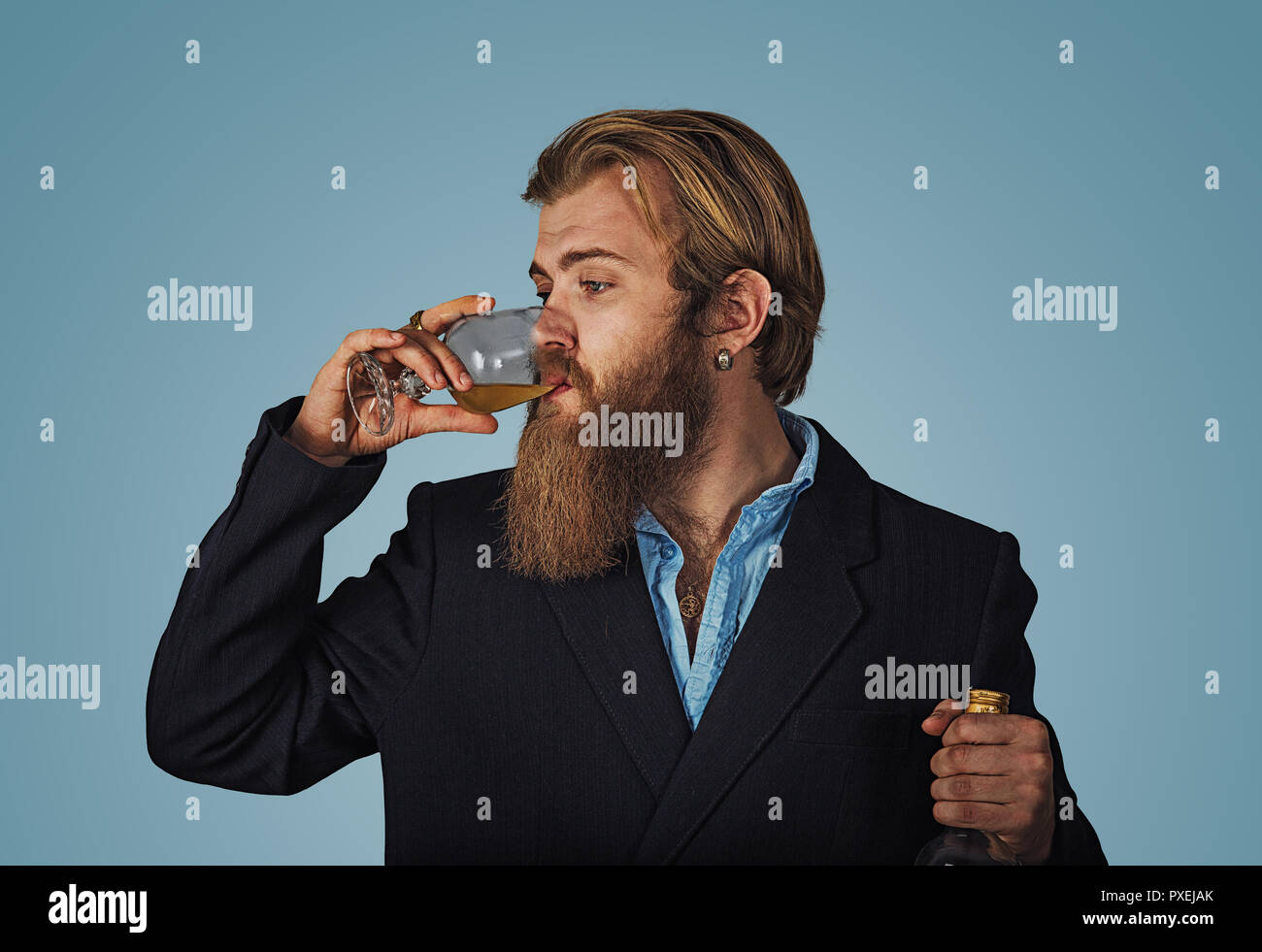 Handsome bearded well-dressed man in jacket holding tasting drinking glass of beverage whiskey alcohol isolated on grey gray studio background wall. d Stock Photo