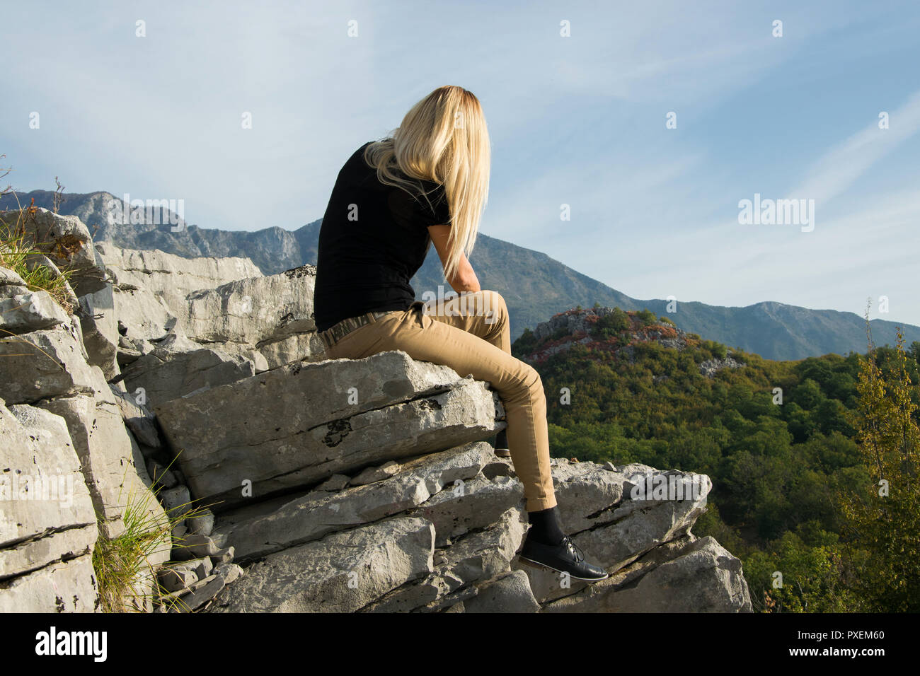 Young blond woman sitting on the edge of the mountain cliff against ...