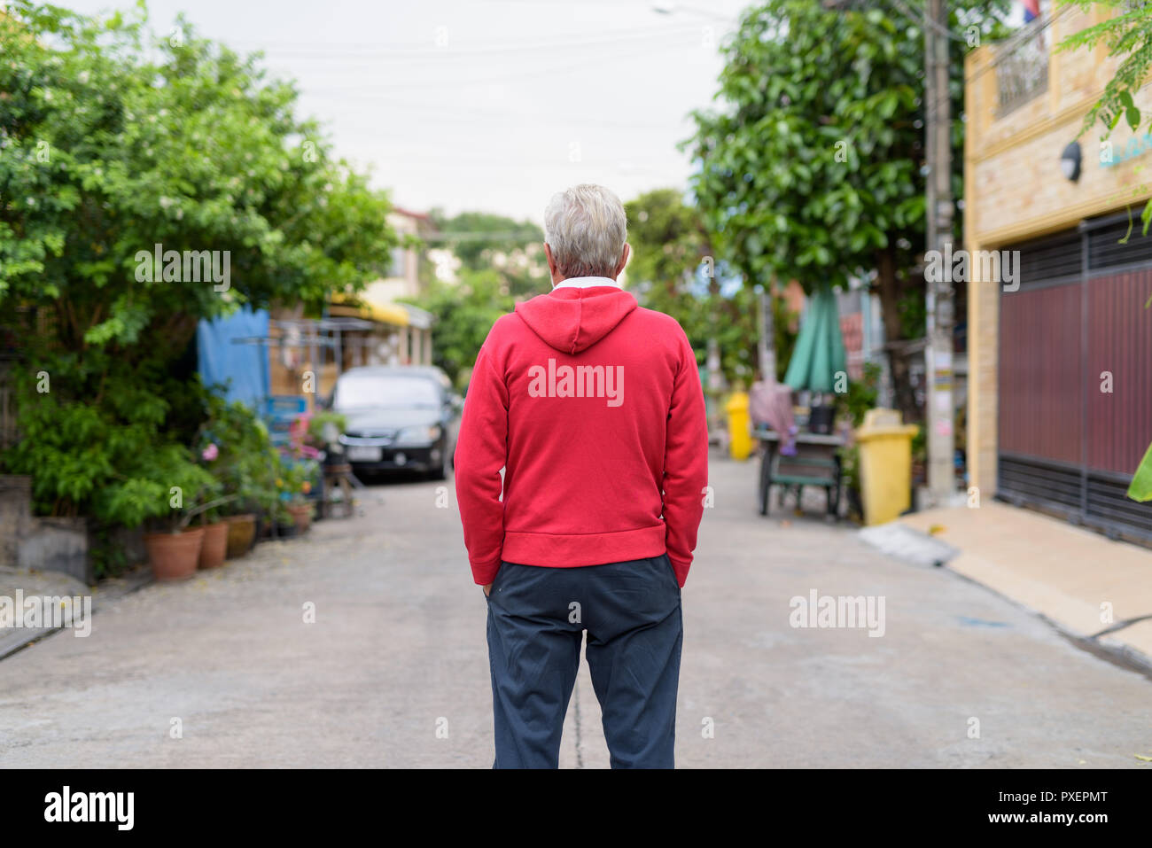 Back view of senior man standing while wearing red jacket outdoo Stock Photo