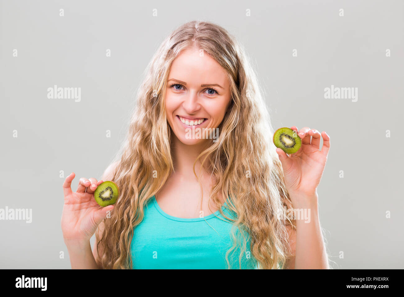 Beautiful young woman showing slices of kiwi on gray background Stock ...