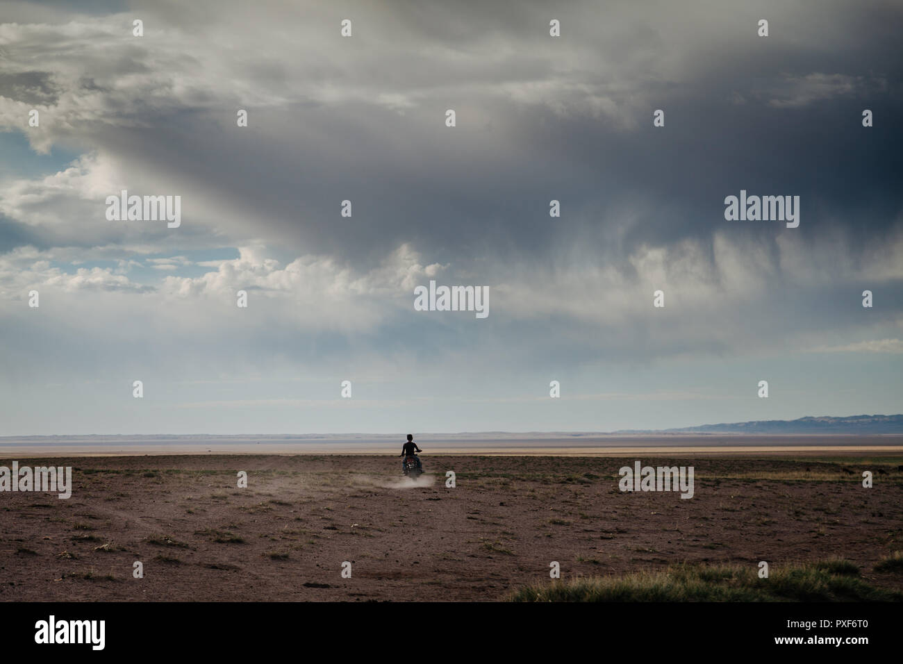 Nomadic boy riding a motorbike across the Gobi desert. Landscape with a dramatic cloudy sky. Govi Altai, Mongolia Stock Photo