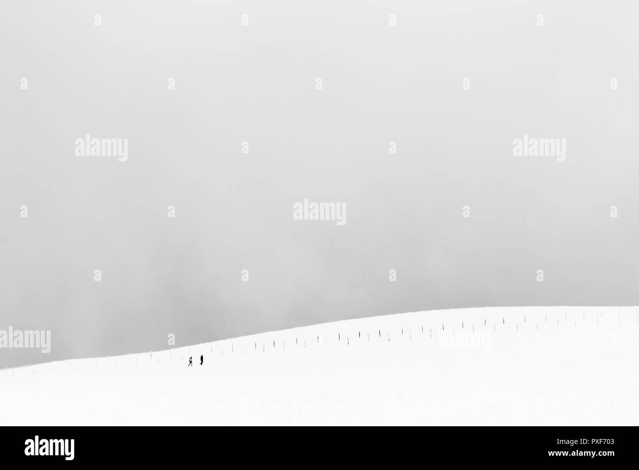 A very minimalistic view of two distant people over a mountain covered by snow, near a fence Stock Photo