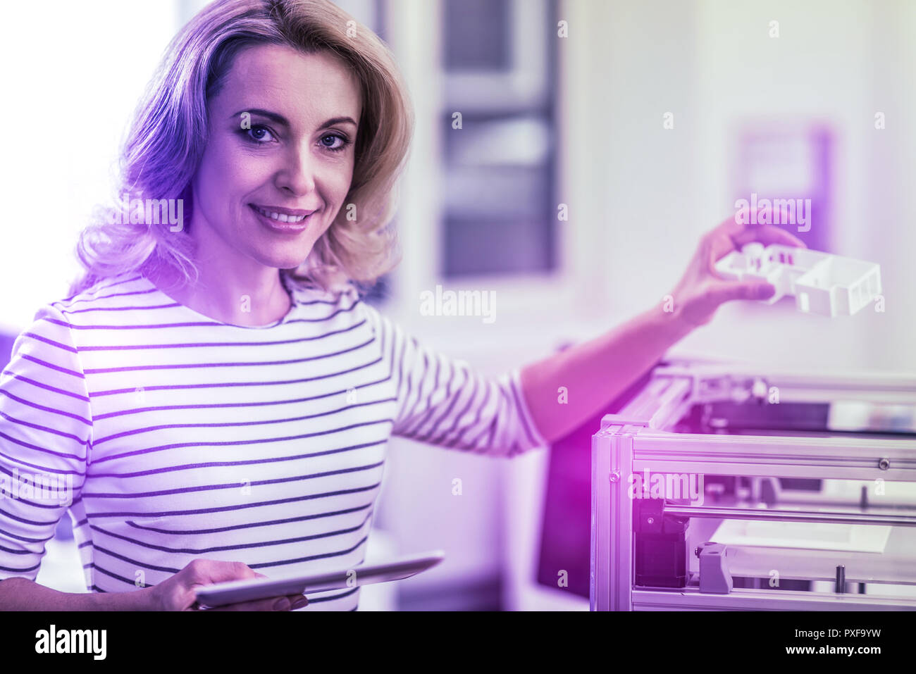 Beautiful blonde-haired interior designer standing near printer working on sketches Stock Photo