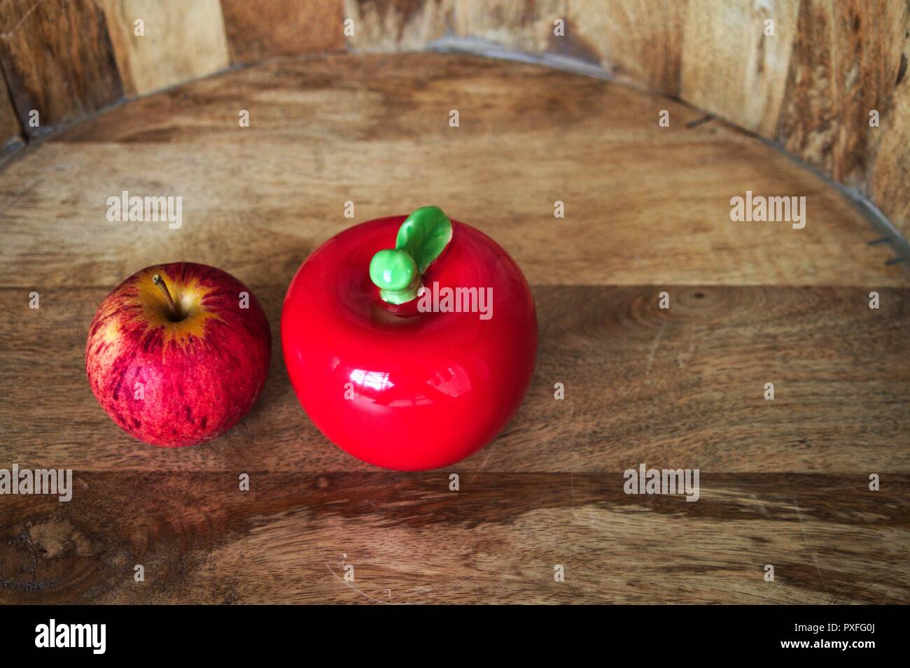 Two red apples, fake and real against a wooden background. Stock Photo