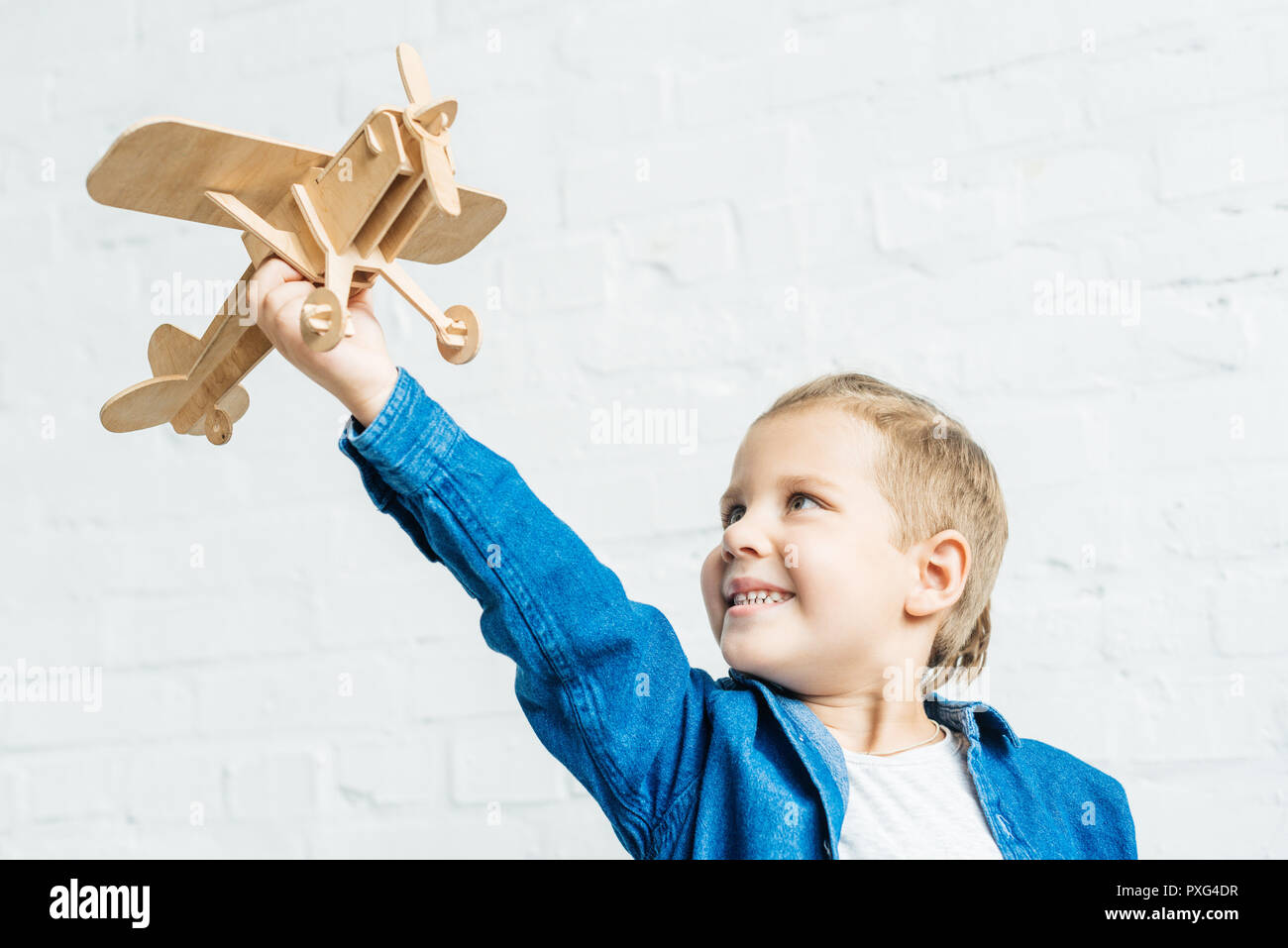 smiling little kid playing with wooden toy airplane in front of white ...