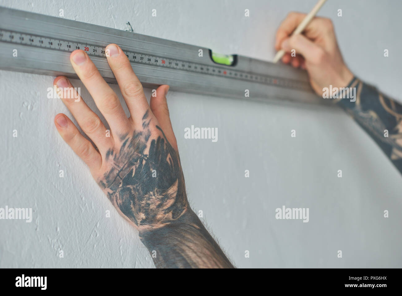 cropped shot of tattooed man holding level tool and marking wall with ...