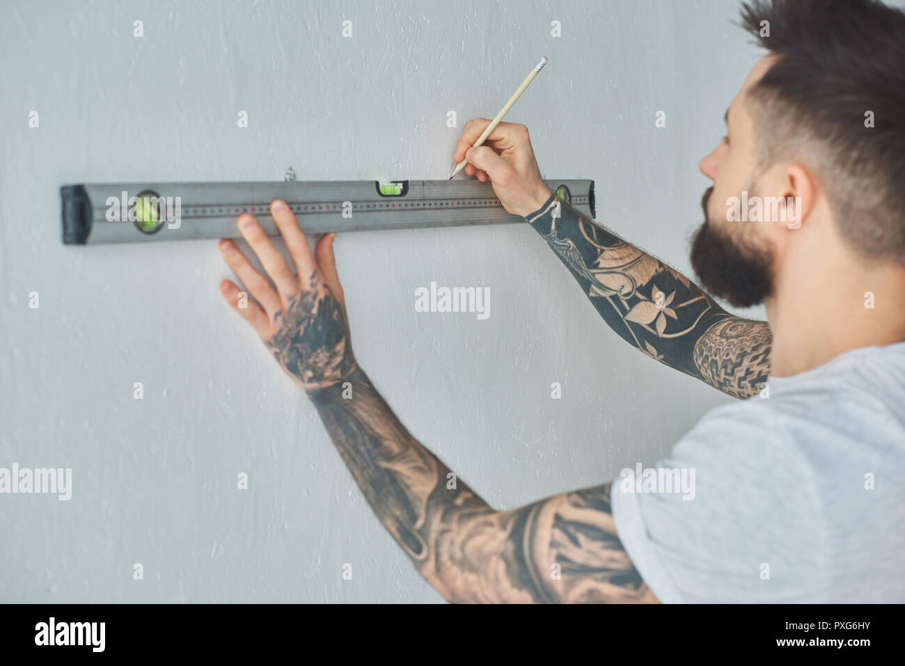 cropped shot of young man holding level tool and marking wall with ...