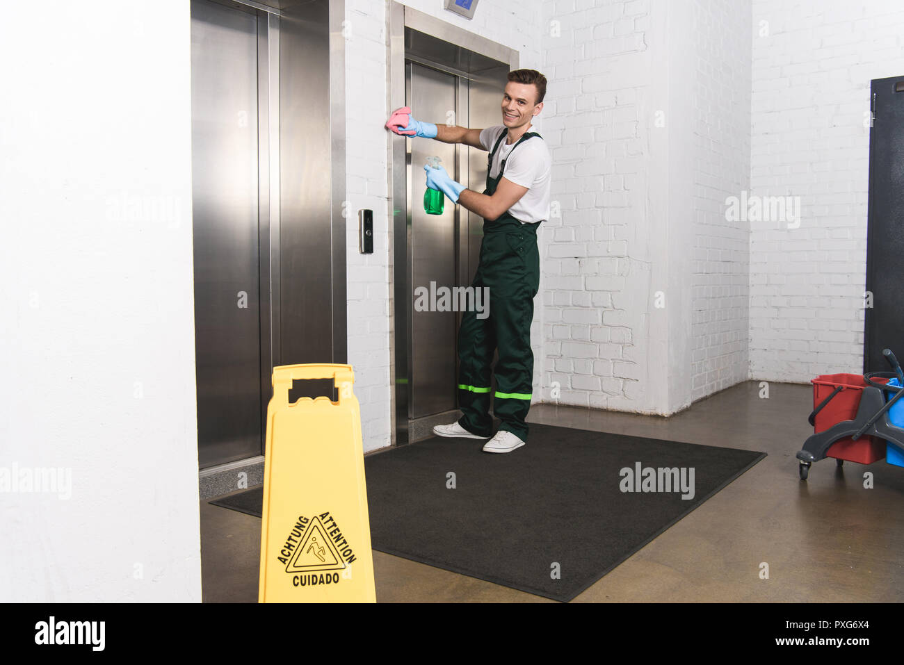 handsome young janitor cleaning elevator and smiling at camera Stock Photo
