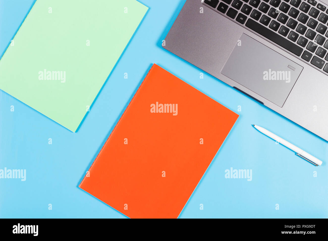 Laptop, open spiral notebook and white pen on blue background. Stock Photo