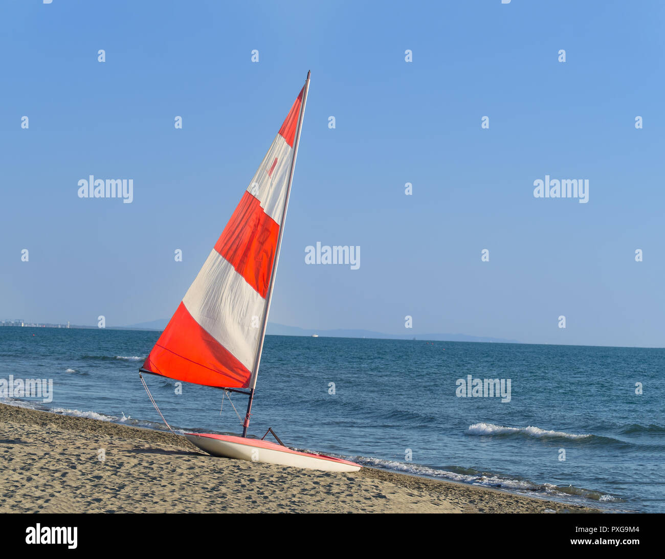 small sail boat with  with red and white  colorful sail on the beach ready for the next ride off the coast Stock Photo