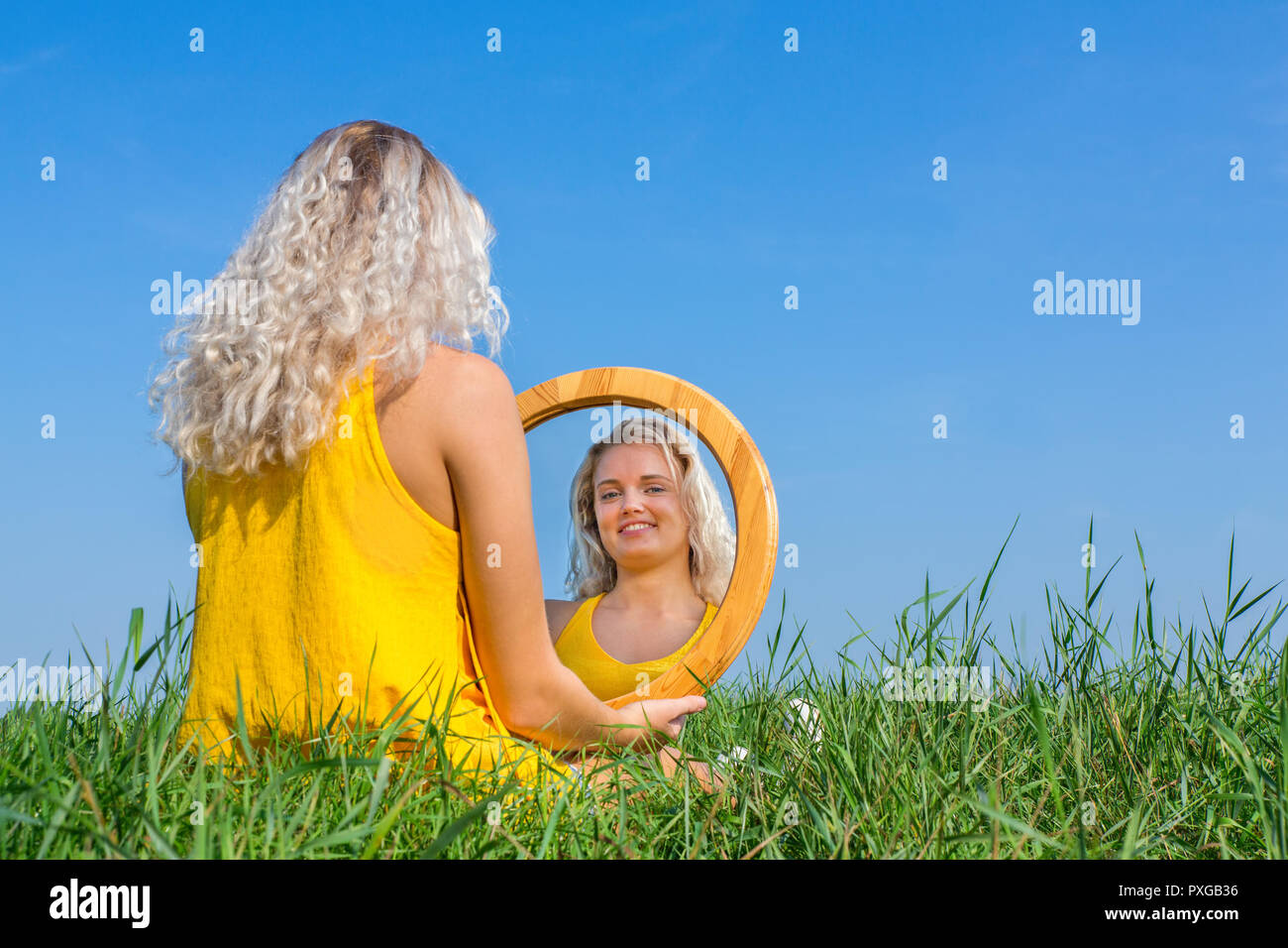 Blond woman sits looking at her mirror image outside Stock Photo