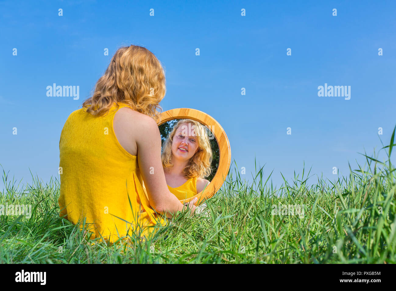 Red-haired woman sits looking at her mirror image outside Stock Photo