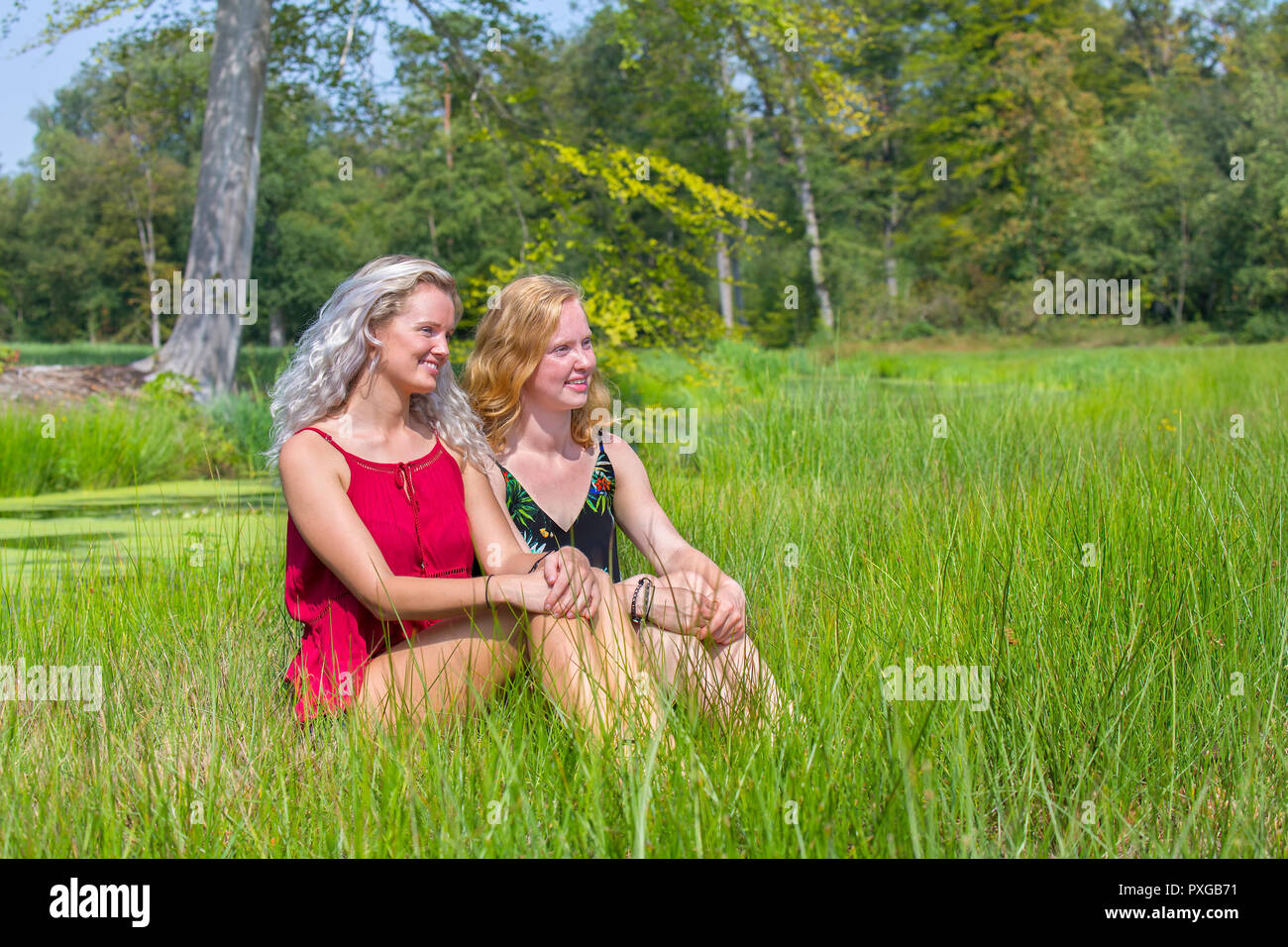 Blond and red-haired woman sitting together in natural meadow Stock Photo