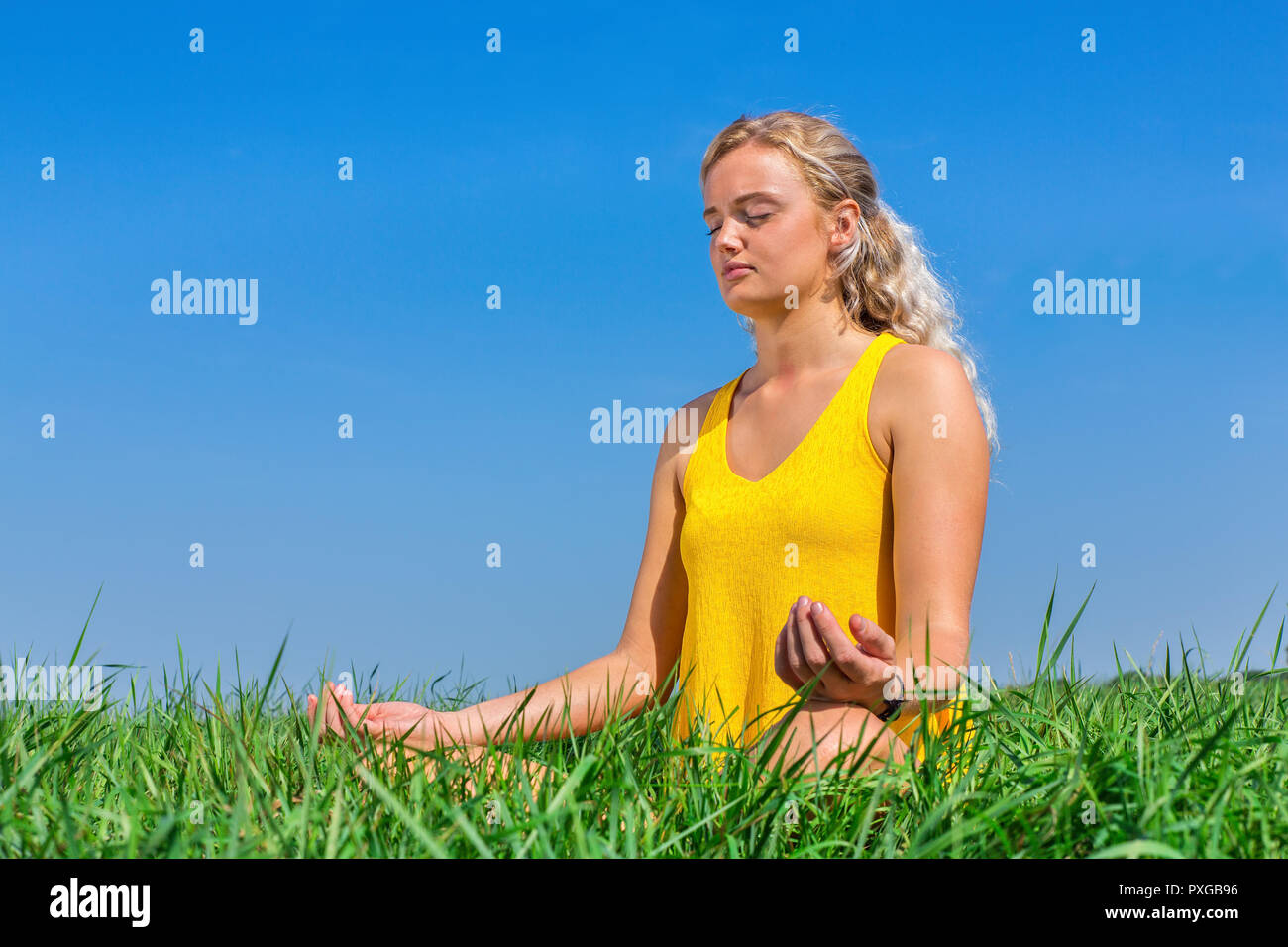 Young blond dutch woman meditating in nature with blue sky Stock Photo