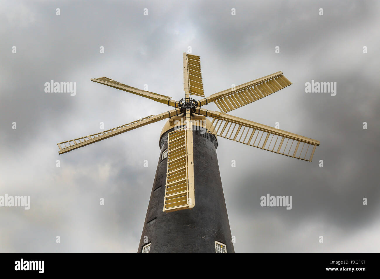 Isolated, six-sailed UK windmill from low-angle viewpoint. Worm's-eye view looking up at windmill blades from below, with dramatic cloudy sky. Stock Photo