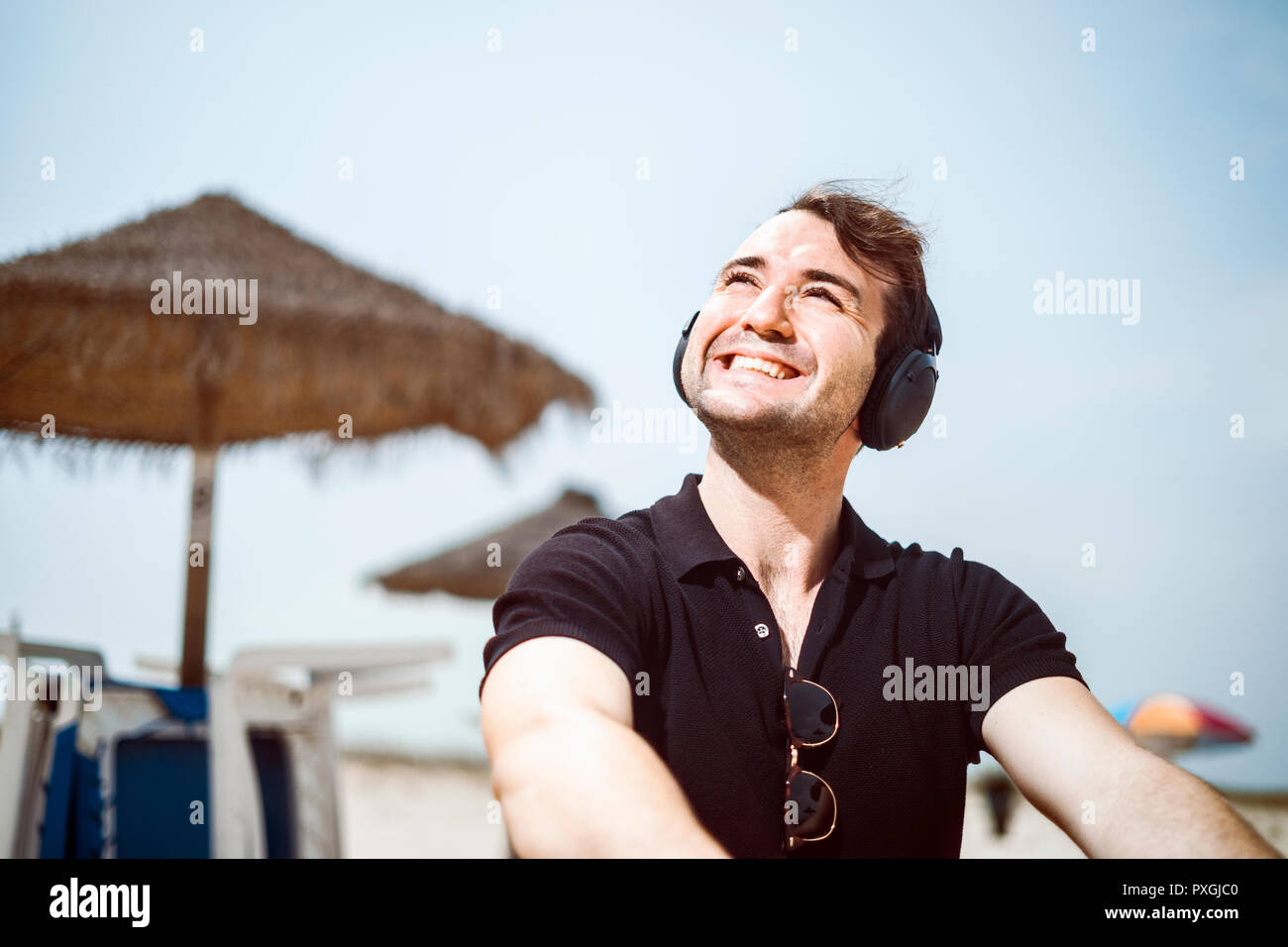 Fashionable man with fancy glasses and headphones sitting on the beach Stock Photo