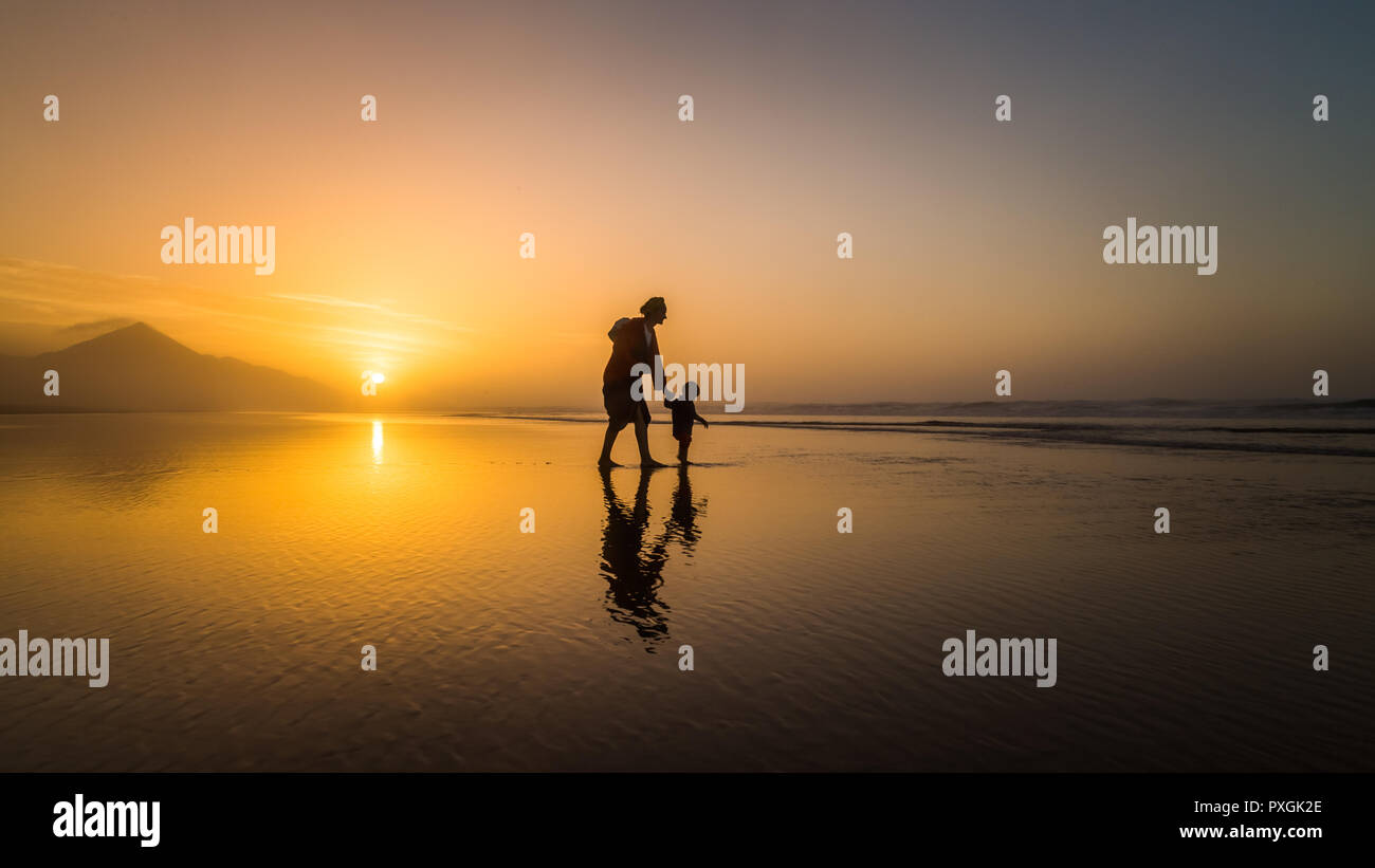 Silhouette of young mother son walking on reflected beach in Cofete, Fuerteventura, Canary Islands, Spain. Stock Photo