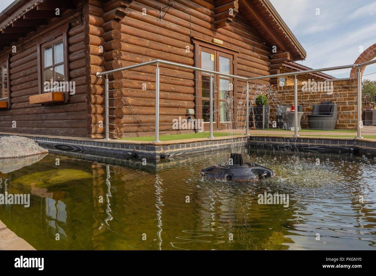 An Image Of A Log Cabin Situated At The Side Of A Fishpond With A