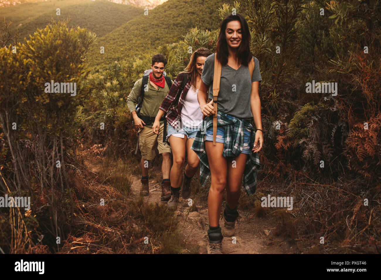 Friends hiking on rugged hilly terrain. Two women with male friend walking on a rocky path on a mountain. Stock Photo
