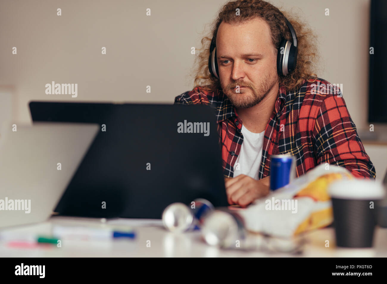 Man busy coding on laptop. Male computer programmer wearing headphones working on laptop at tech startup. Stock Photo