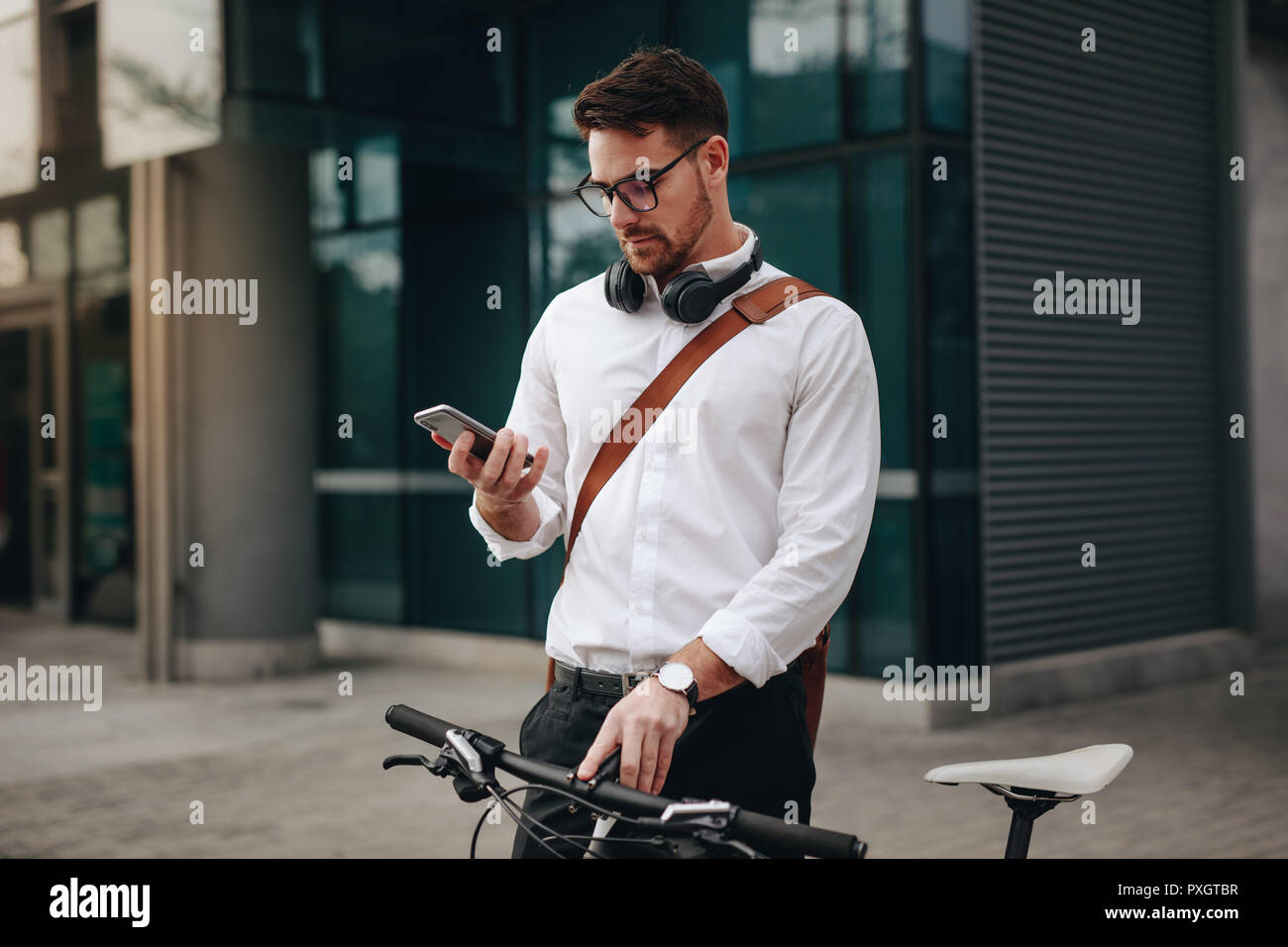 Man checking his mobile phone standing on street with his bicycle while commuting to office. Businessman using mobile phone while going to office. Stock Photo