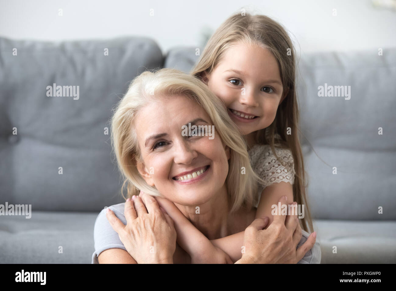 Portrait of smiling granddaughter piggyback grandmother at home Stock Photo