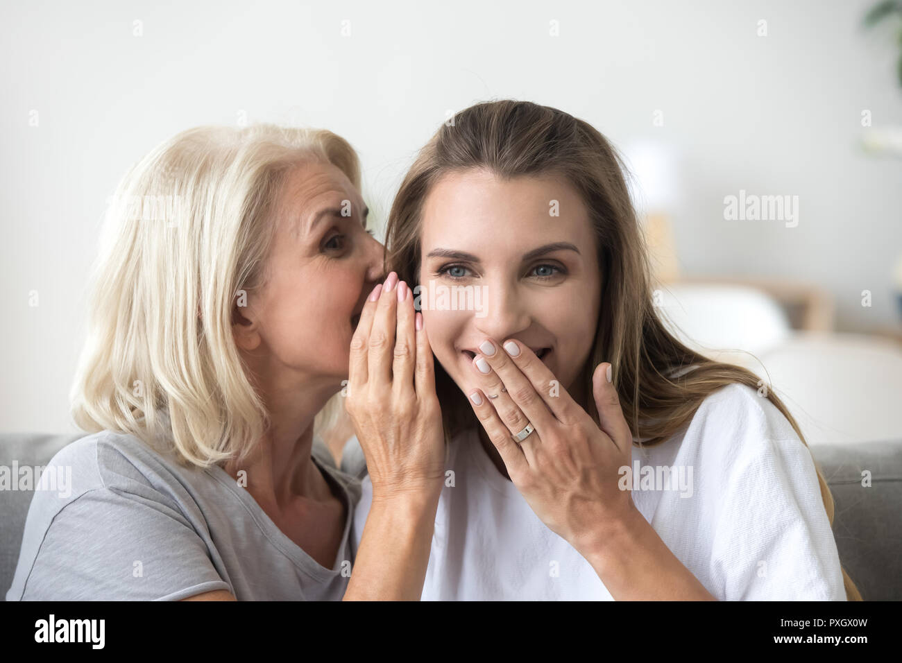 Excited aged mother share secret with adult daughter  Stock Photo