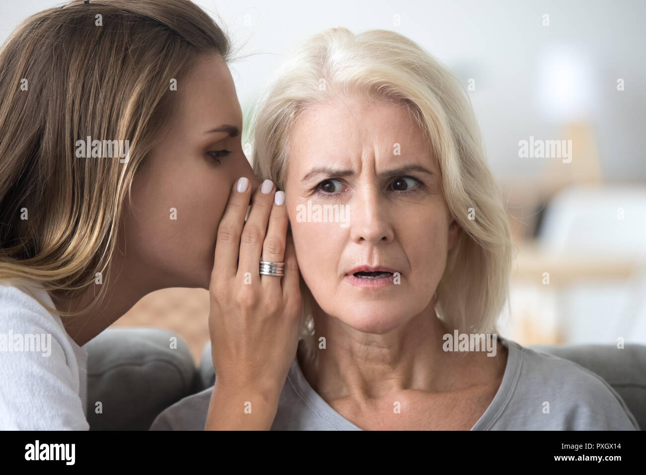 Adult daughter share secret with surprised aged mom Stock Photo