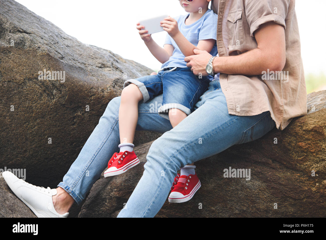 cropped image of father and son using smartphone on stones at park Stock Photo