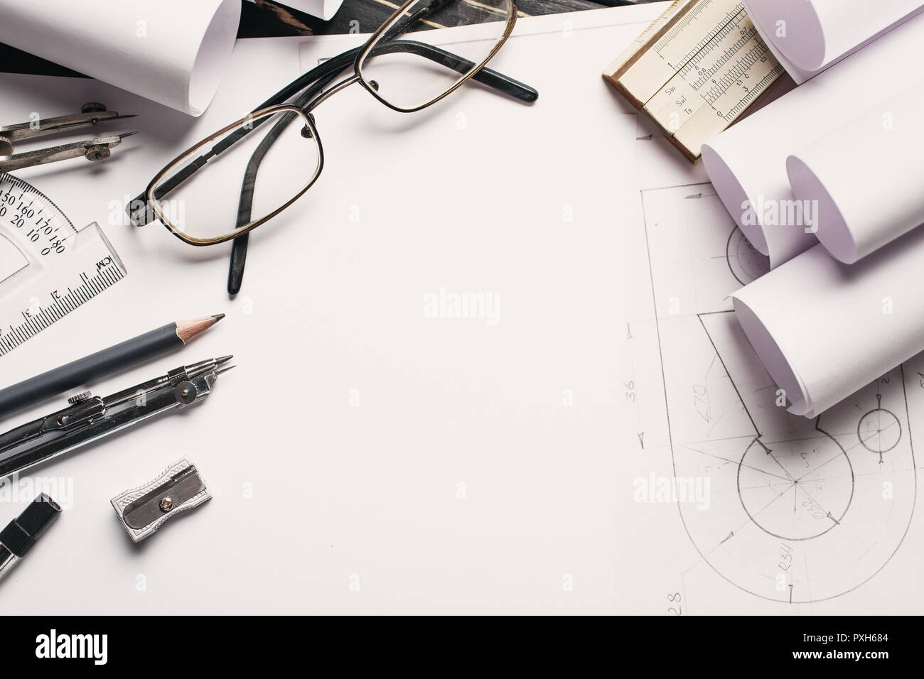 On the wooden table there are drawings, compasses, pencil, elastic, ruler, sharpener and glasses. Stock Photo