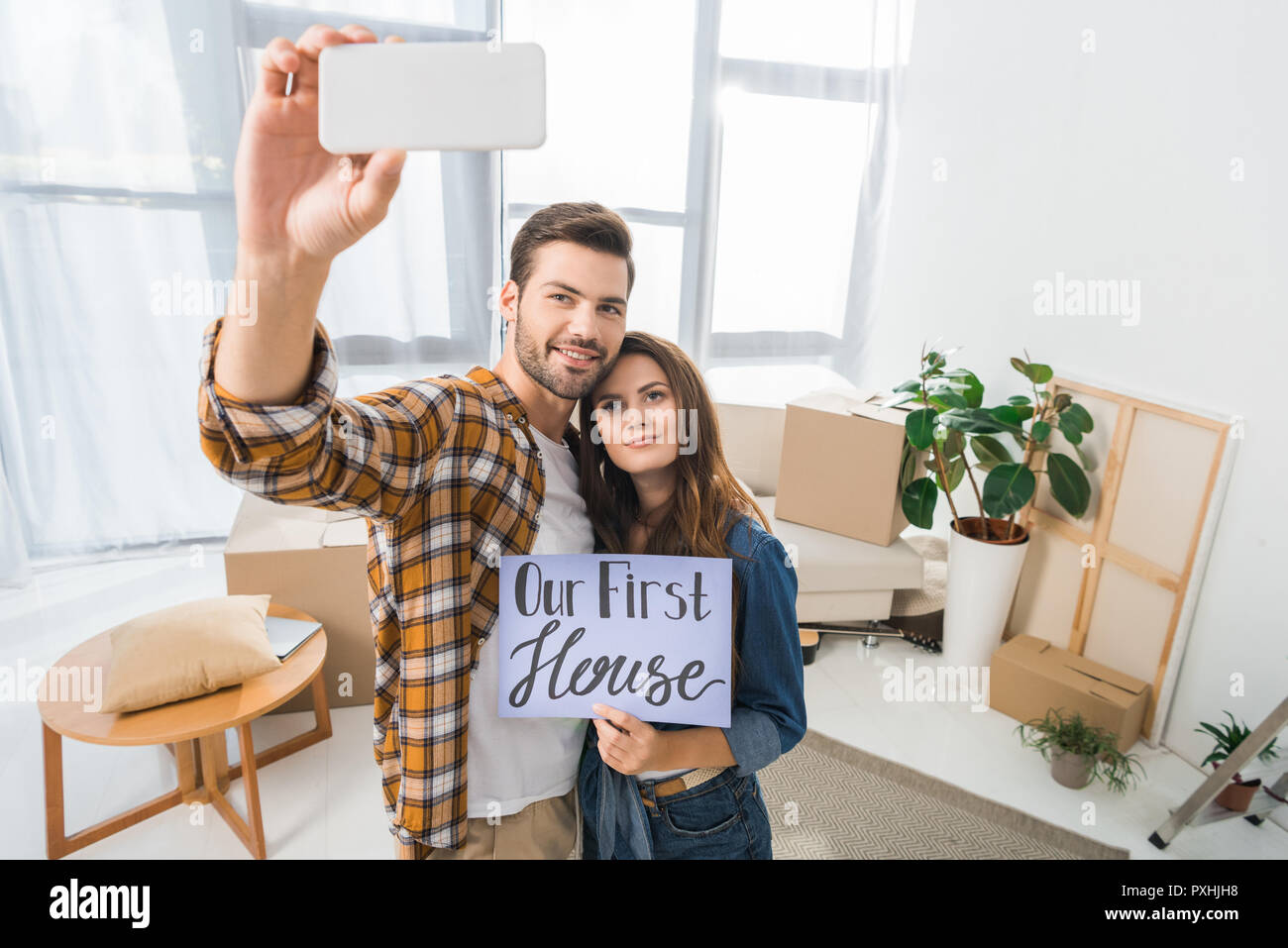 portrait of young couple with our first house card taking selfie on smartphone, moving home concept Stock Photo