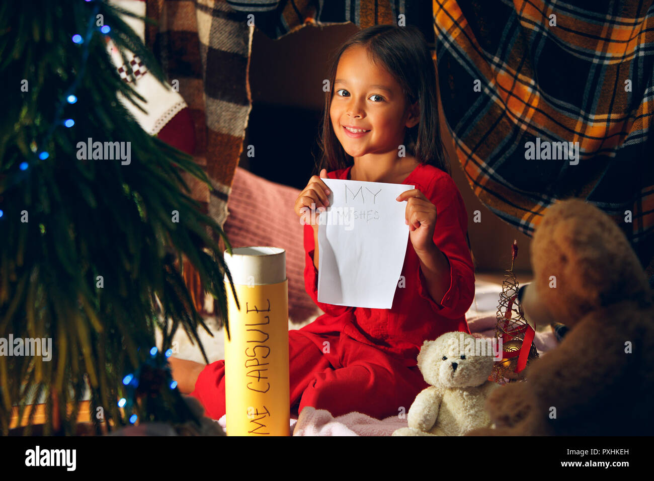 Merry Christmas and Happy Holidays. Cute little child girl writes the letter to Santa Claus near Christmas tree at home indoor. The holiday, childhood, winter, celebration concept Stock Photo
