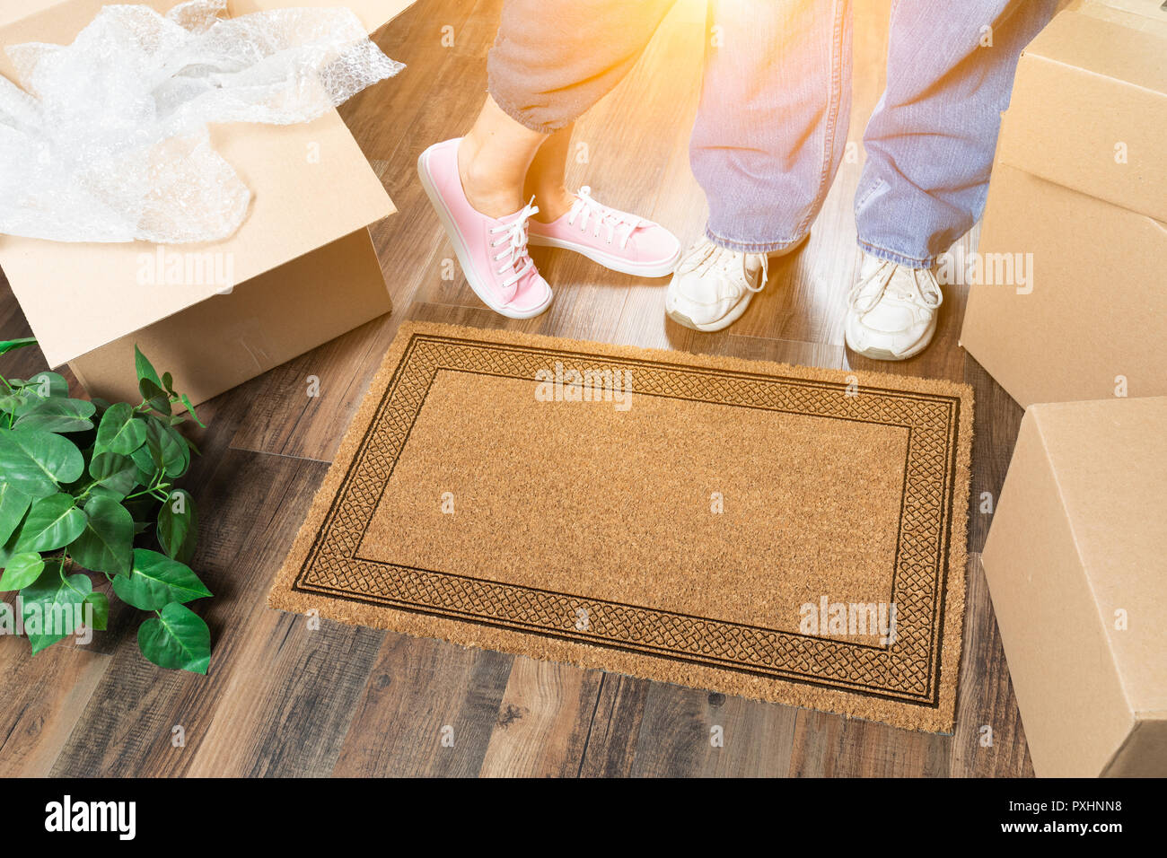Man and Woman Standing Near Blank Welcome Mat, Moving Boxes and Plant. Stock Photo