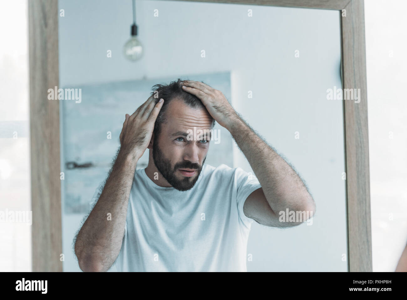 middle aged man with alopecia looking at mirror, hair loss concept Stock Photo