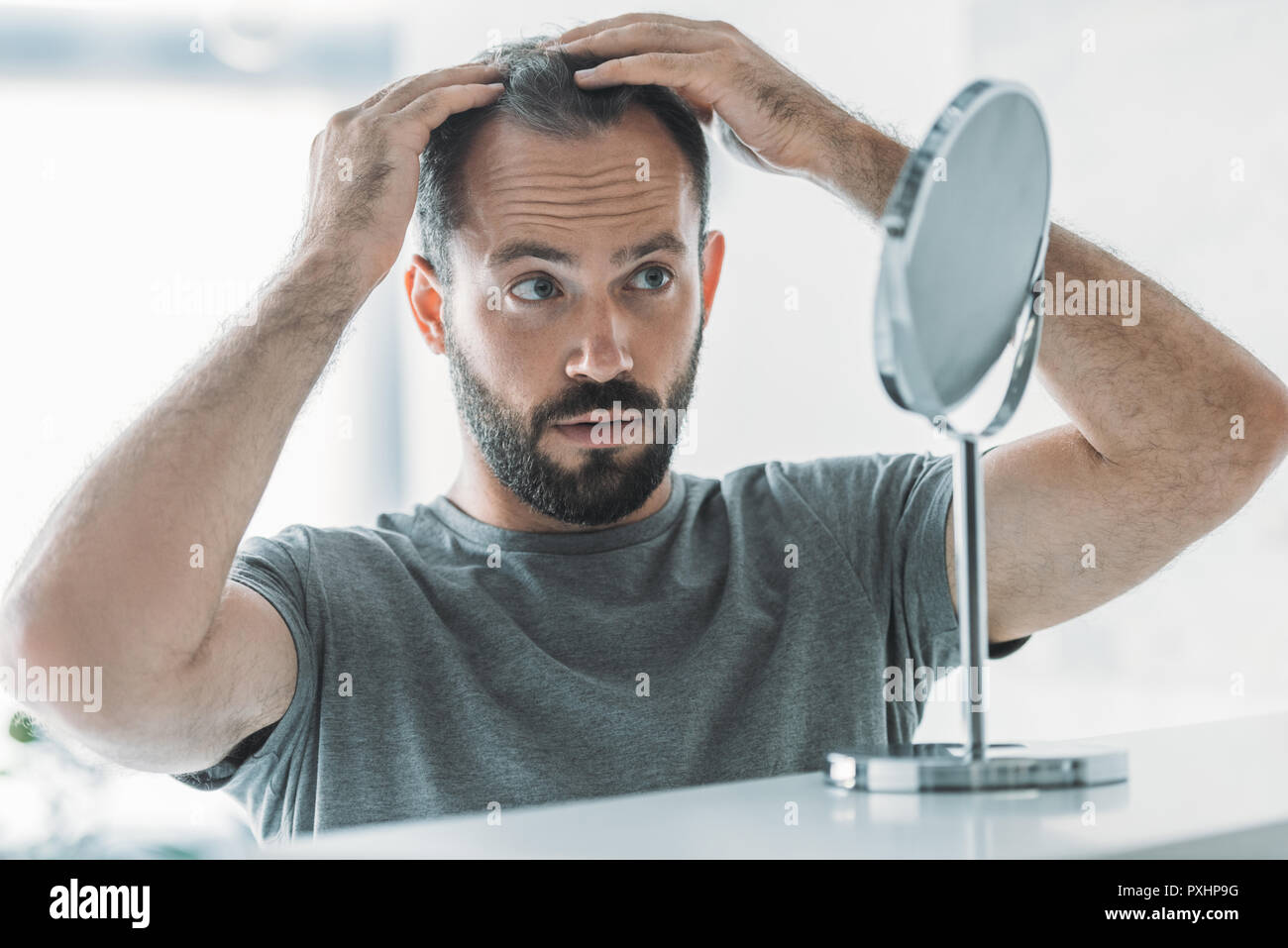 bearded mid adult man with alopecia looking at mirror, hair loss concept Stock Photo