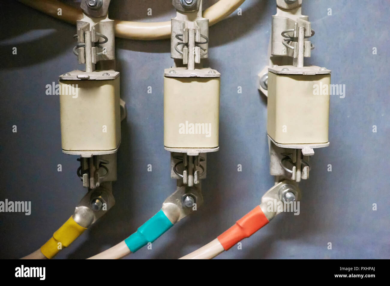 Three trains of high-voltage fuses are connected to the multi-colored wires. Industrial background. Stock Photo