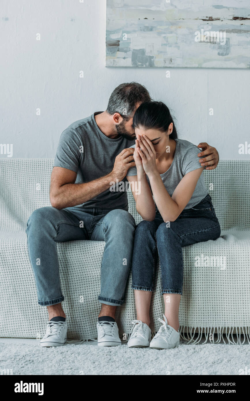 upset young man supporting depressed girlfriend while sitting together on couch Stock Photo