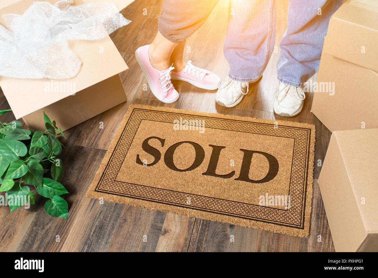 Man and Woman Standing Near Sold Welcome Mat, Moving Boxes and Plant. Stock Photo