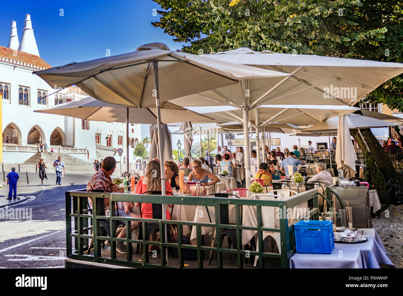 Tourists eating and drinking in an outside restaurant with the royal palace in the background, Sintra Portugal Stock Photo