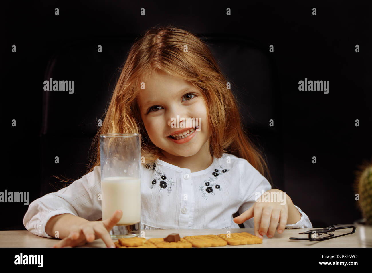 Happy beautiful little girl having a snack with milk and cookies Stock