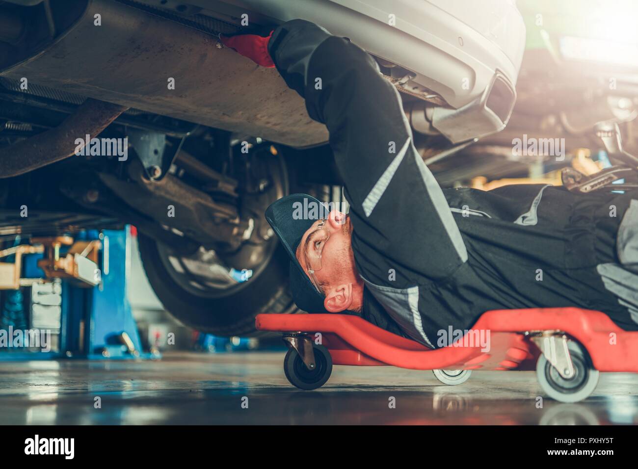 Caucasian Car Mechanic in His 30s Under the Car on the Mechanics