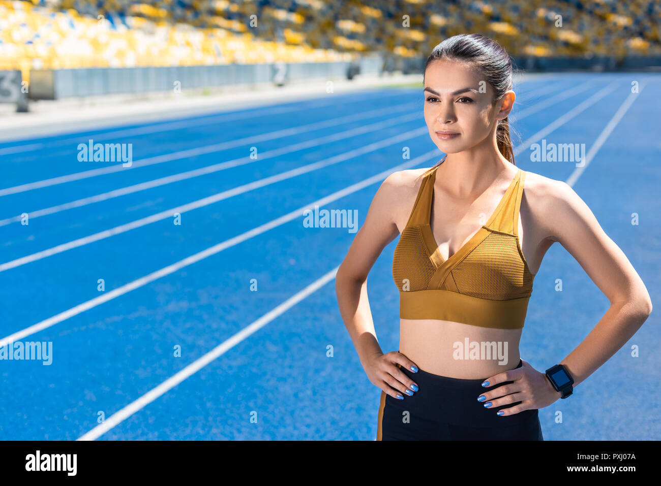 athletic female jogger with arms akimbo on running track at sports stadium Stock Photo