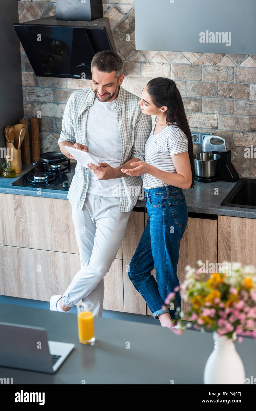 married couple using digital tablet together in kitchen, smart home concept Stock Photo