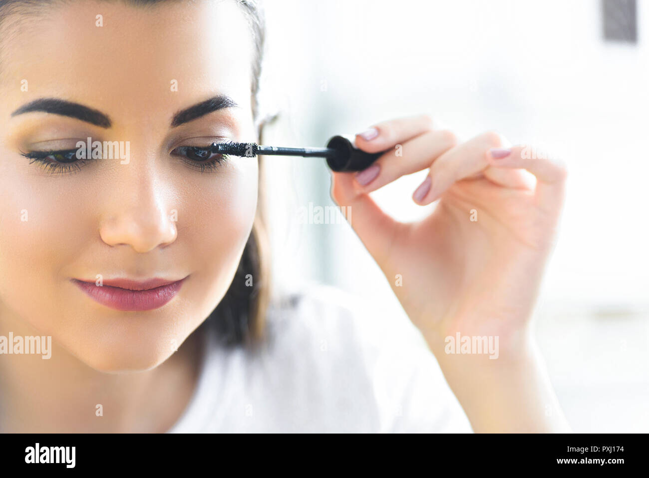 portrait of attractive young woman applying black mascara on eyelashes ...